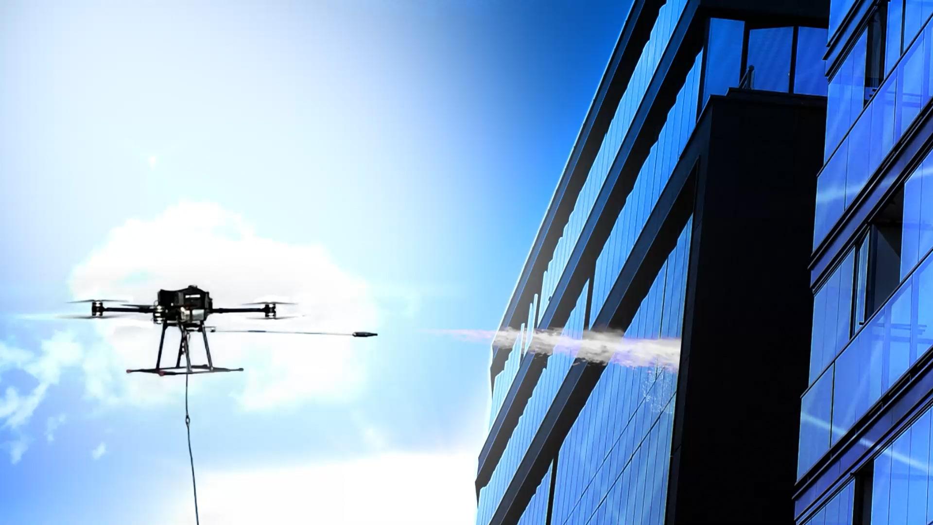 Drone equipped with a high-pressure washer cleaning a large mirrored building on a sunny day.