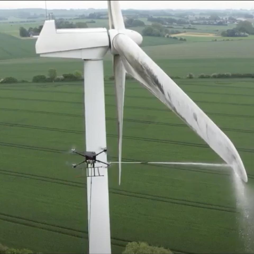 Specialized training and support: Drone cleaning a wind energy tower with a high-pressure washing system